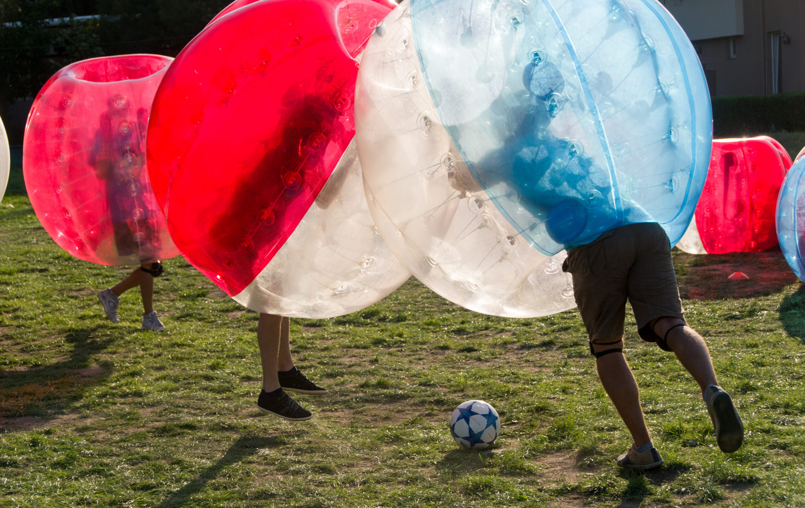 Teenagers play in Bubble bump, new and fun team game outdoor. Children are inside of blown plastic transparent bubble shock each other with fun. Out of focus park zone is at background